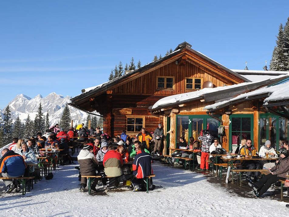 Holzhütte im Schnee mit Terrasse voll mit Menschen | © Weitmoosalm
