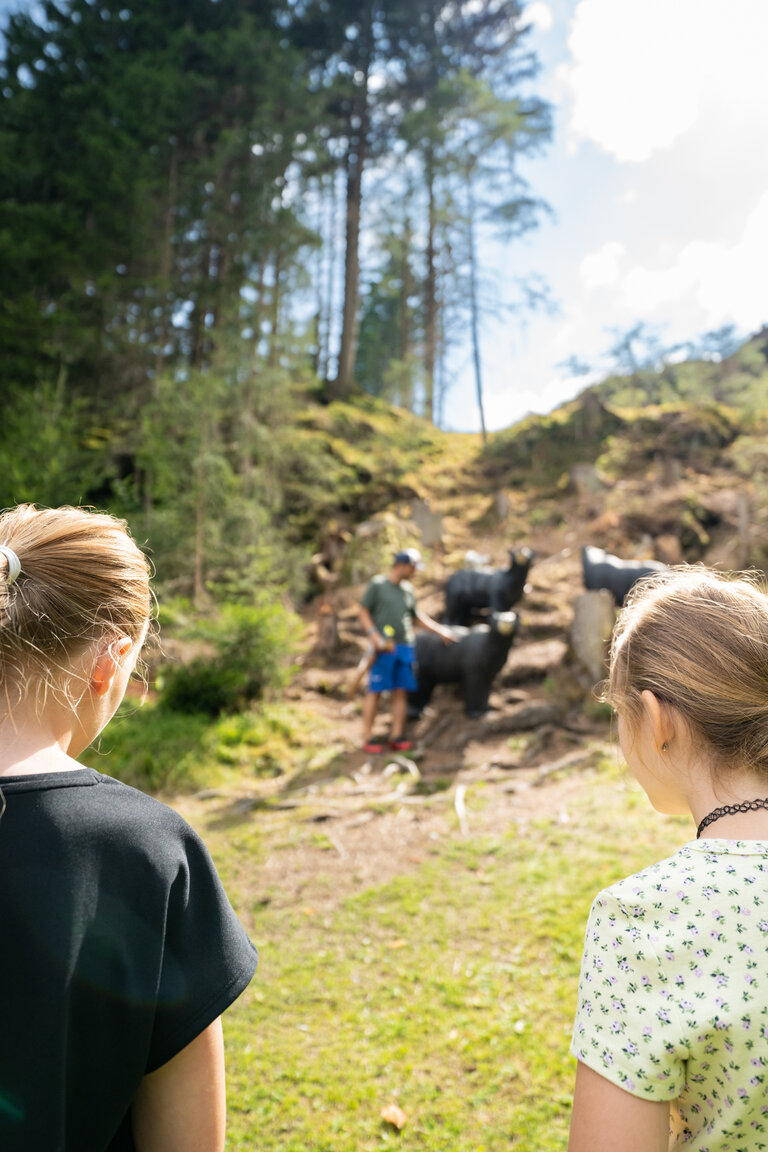 Zwei Kinder beobachten Mann bei 3D-Zielobjekten für Bogenschießen auf Waldlichtung | © TVB/Laura Passenbrunner